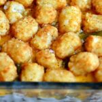 A golden, cheesy Tater Tot Casserole baked in a white dish with crispy tots on top