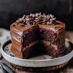 A slice of super moist chocolate cake layered with rich chocolate ganache on a white dessert plate