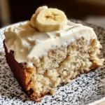 A slice of Banana Bread Cake with thick cream cheese frosting and banana slices on top.