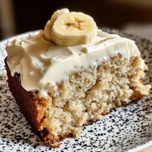 A slice of Banana Bread Cake with thick cream cheese frosting and banana slices on top.
