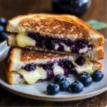 A crispy Blueberry Grilled Cheese Sandwich cut in half showing melted Gruyere cheese and fresh blueberries.