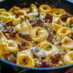 A creamy bowl of Cheesesteak Tortellini with melted provolone sauce and sliced bell peppers.