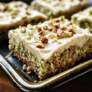 A plate of moist Zucchini Bars topped with creamy brown butter frosting, garnished with chopped pecans.