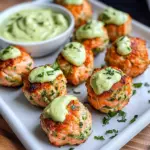 Baked salmon meatballs drizzled with creamy avocado sauce on a white plate
