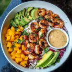 Colorful shrimp bowl topped with avocado, mango salsa, and lime wedges in a white bowl