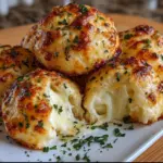 A plate of golden-brown Gooey Mozzarella Biscuit Bombs oozing with melted cheese