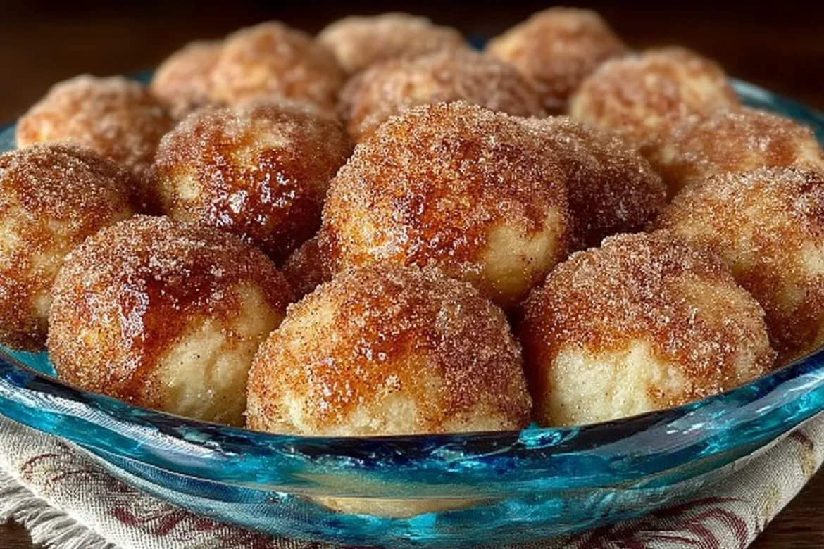 A plate of golden-brown cinnamon sugar donut holes with a dusting of sugar and a side of melted butter.