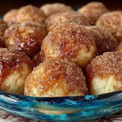 A plate of golden-brown cinnamon sugar donut holes with a dusting of sugar and a side of melted butter.