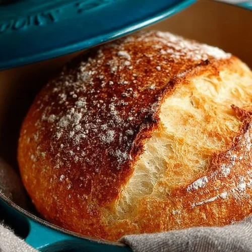 Freshly baked easy no knead bread in a Dutch oven on a wooden table
