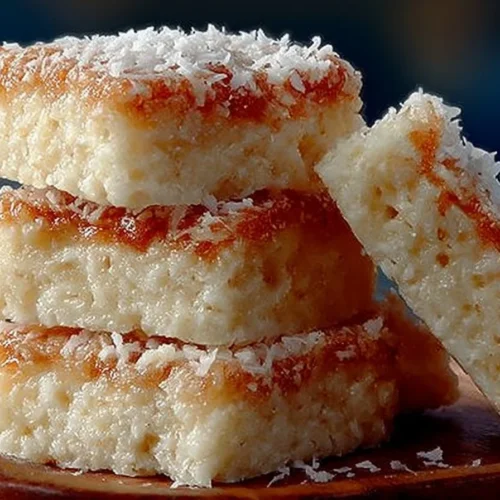 No-bake coconut bars stacked on a plate, showcasing their texture and coconut flakes.