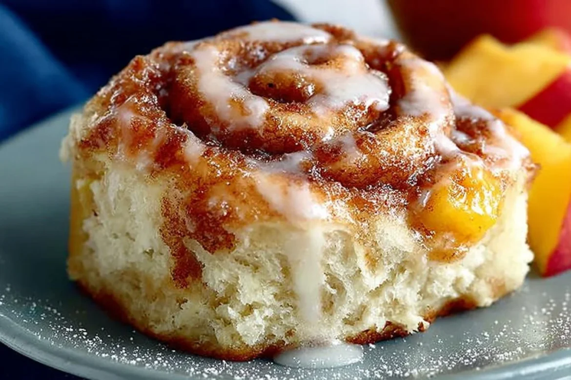 Freshly baked Peach Cinnamon Rolls topped with glaze and sliced peaches.