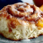 Freshly baked Peach Cinnamon Rolls topped with glaze and sliced peaches.