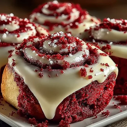 Red velvet cinnamon rolls topped with cream cheese icing on a plate