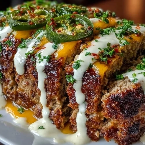 Smoky Jalapeño Popper Meatloaf drizzled with creamy ranch dressing on a plate.
